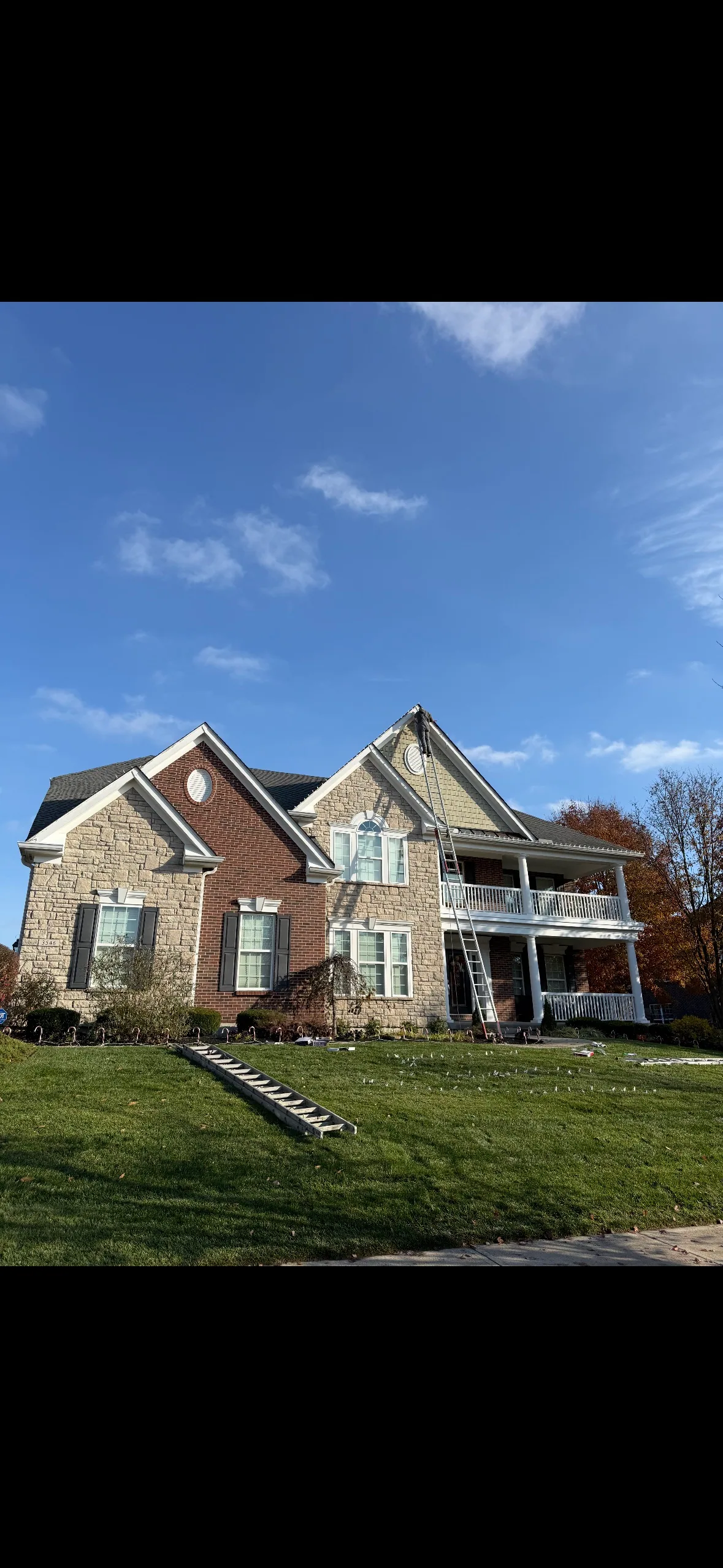 Christmas lighting installation in progress with ladders along the front of the house